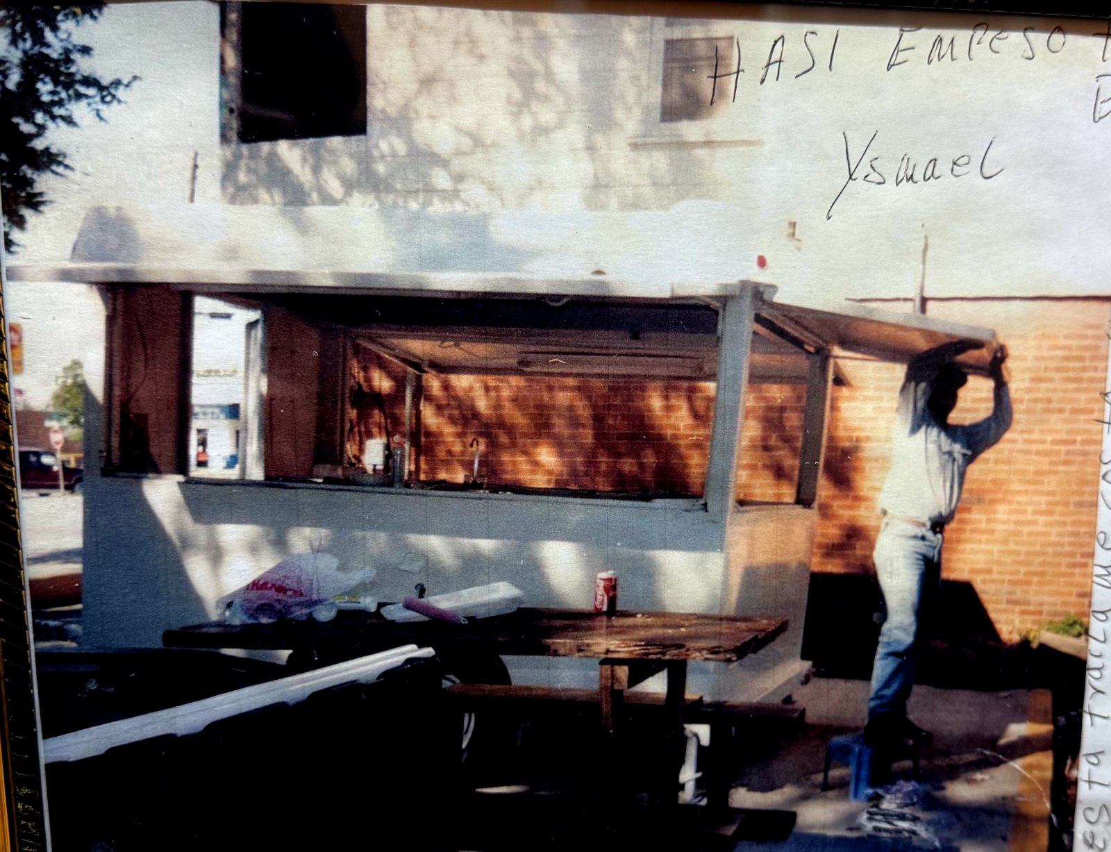 Framed photo of the trailer under construction, a man on a step stool holding up the roof beam, with a handwritten note: así empezó Tacos La Bala